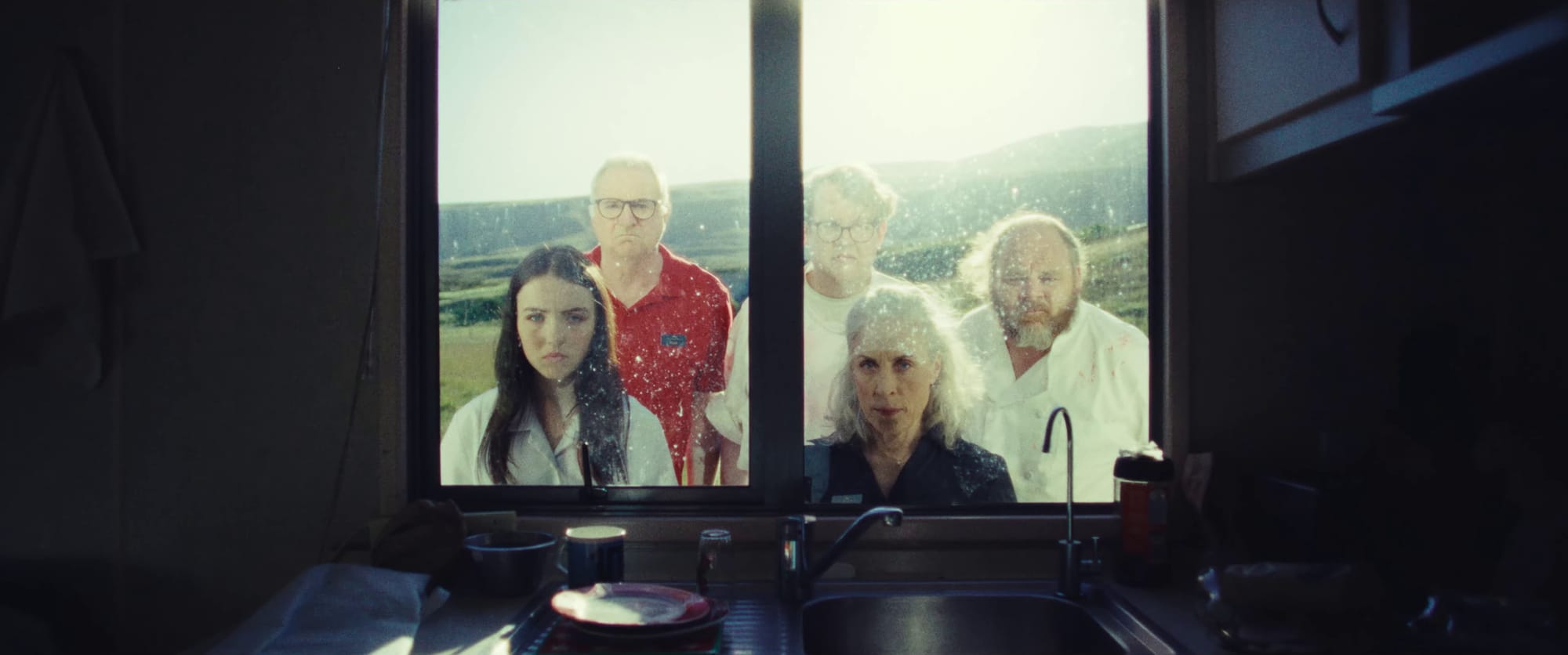 Shadowy shot of five people staring ominously through a dirty kitchen window