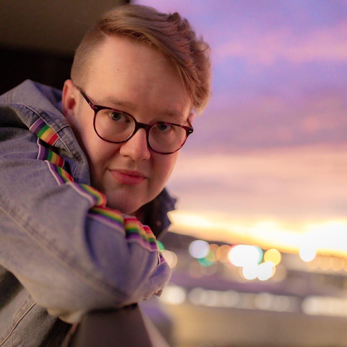Brooding, ethereal photo. Mark (against a fluffy sunset) rests his rainbow-striped denim sleeve and looks at the camera.