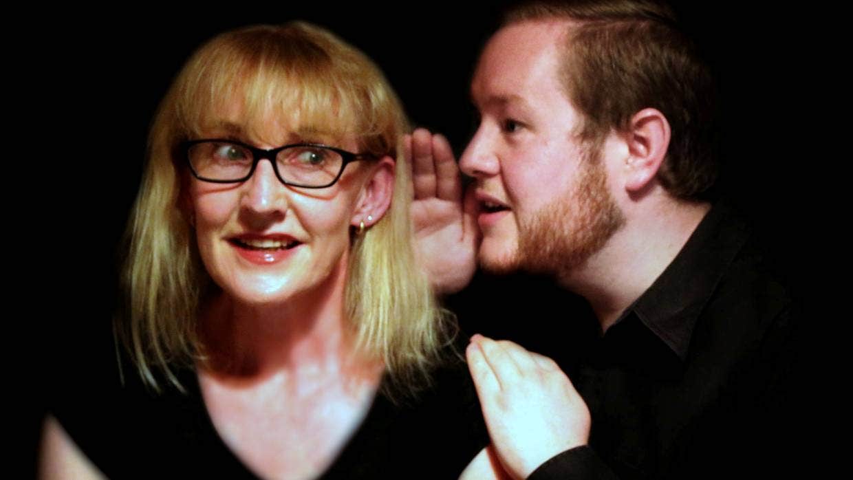 A bearded man whispers into a woman's ear.