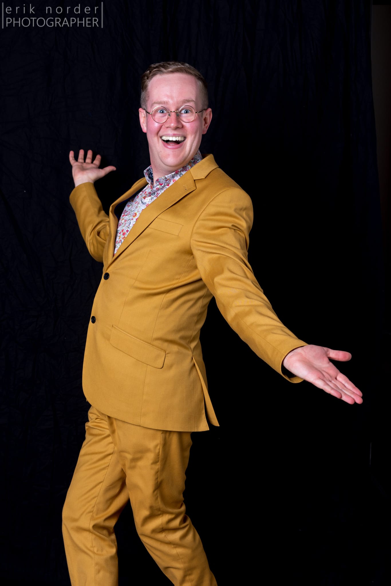 Mark Darbyshire wearing a bright mustard suit, grinning, arms held wide. By Erik Norder Photography.