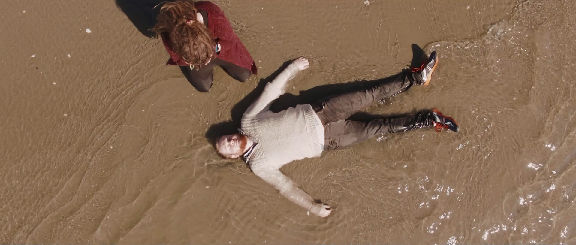 Birds-eye view of Mark Darbyshire lying dead in the shallows at the beach next to his grieving partner